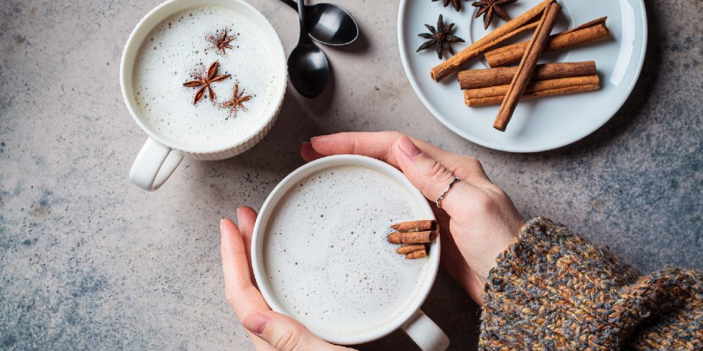 Homemade chai latte with cinnamon and star anise in white cup in hands