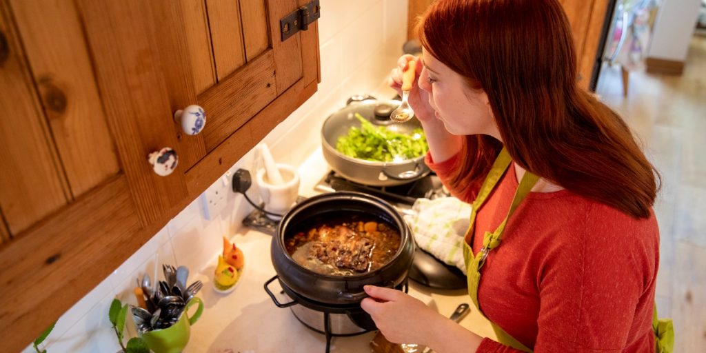 Overhead shot of a teenage Caucasian girl standing in the kitchen over the slow cooker tasting the casserole from a teaspoon