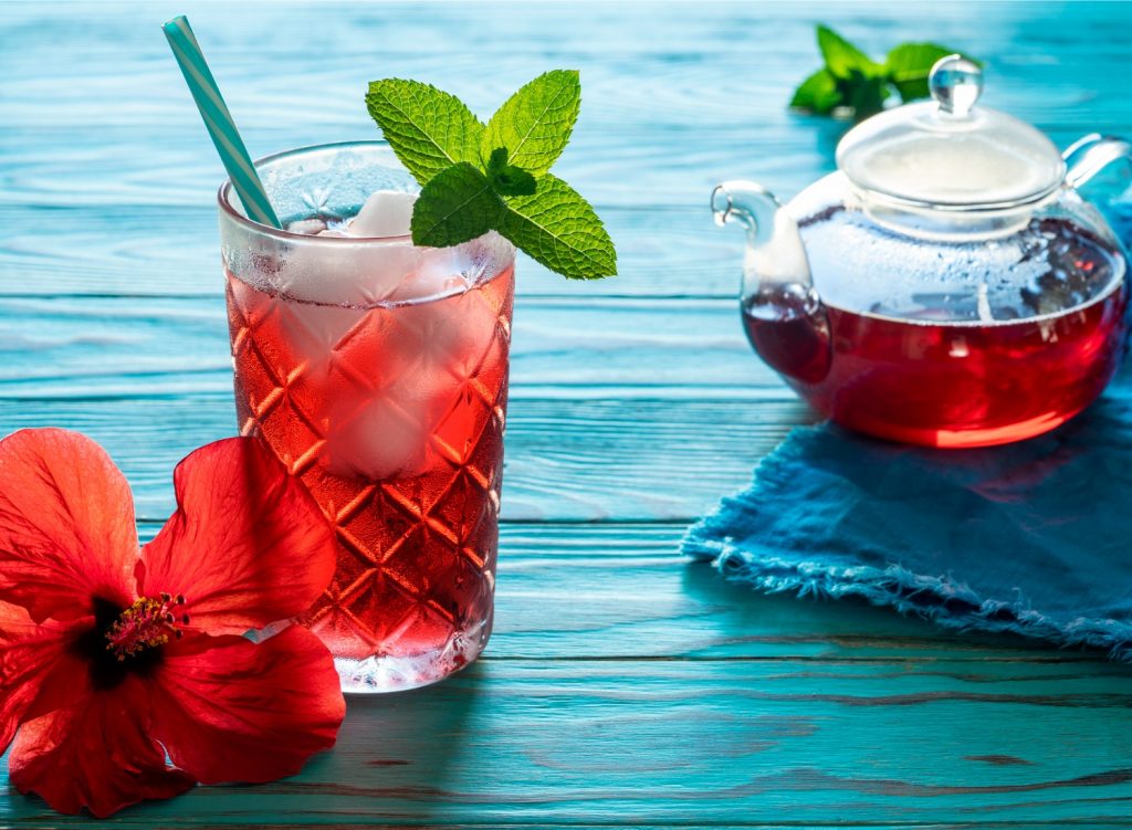 Glass of hibiscus tea next to a teapot