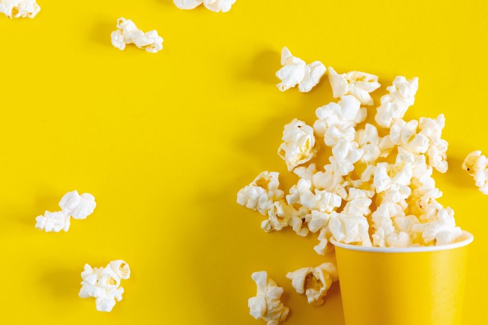 Popcorn spilled out of a yellow cup on a yellow background.