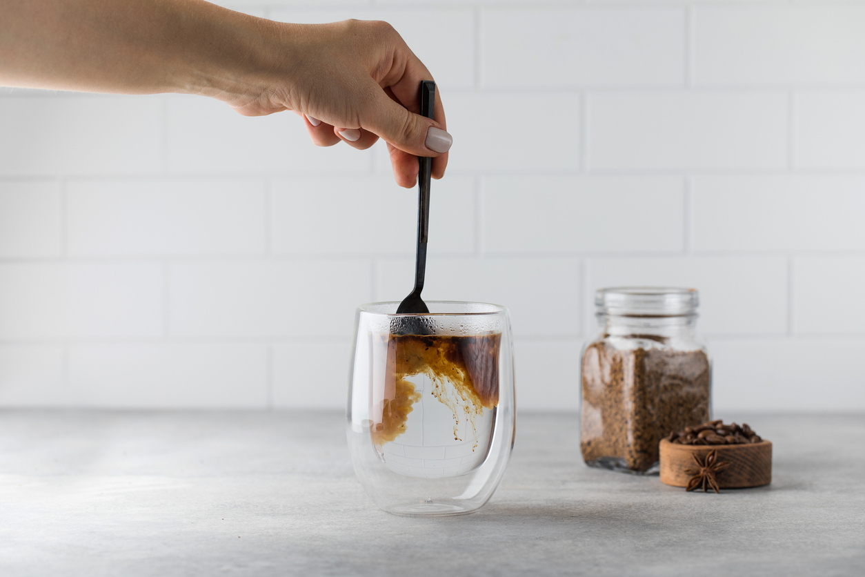 A person scooping instant coffee into a nearby mug.